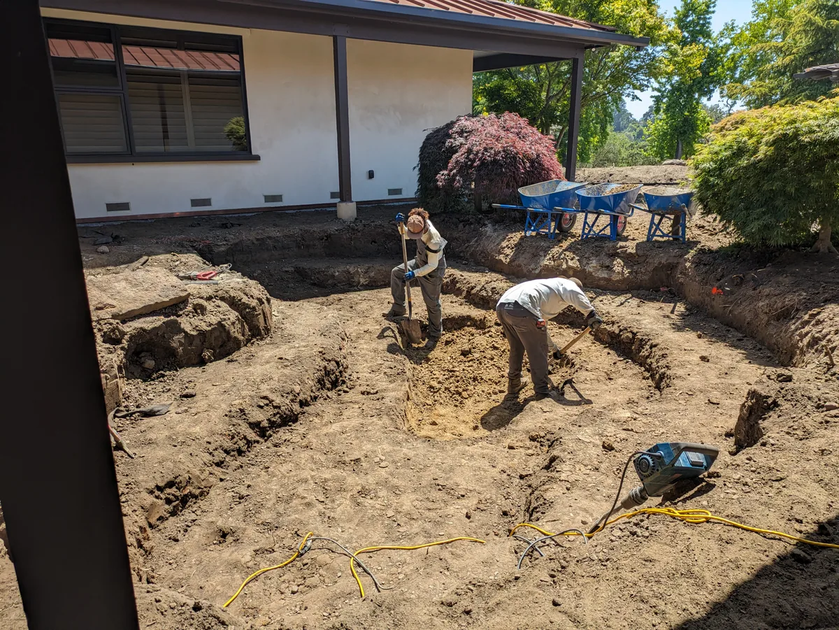 Two Water & Stone crew members digging and shaping a new pond