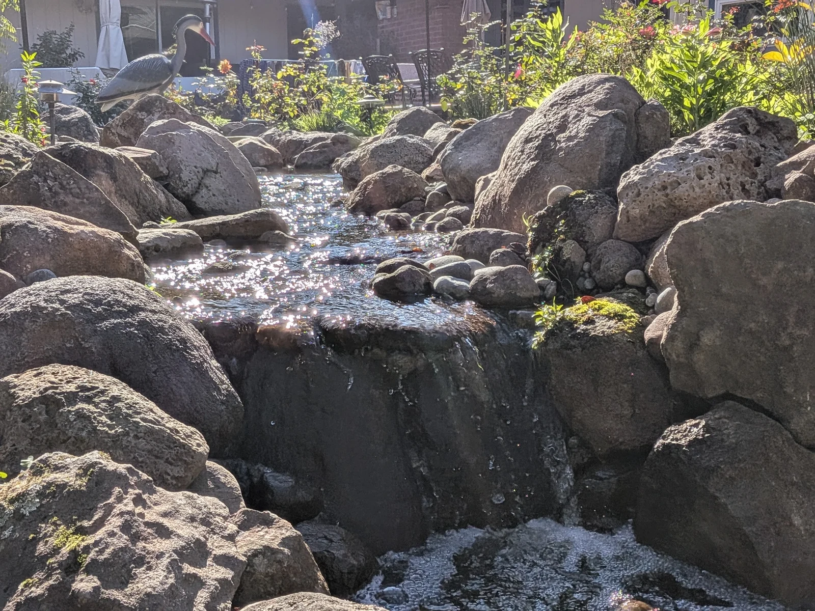 Sunlit stream and waterfall winding between hand-set boulders and garden planting